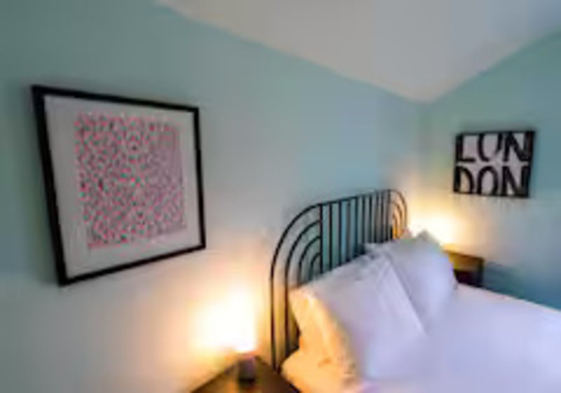 Bedroom with metal bed frame, white bedding, wall art, and bedside lamp lighting