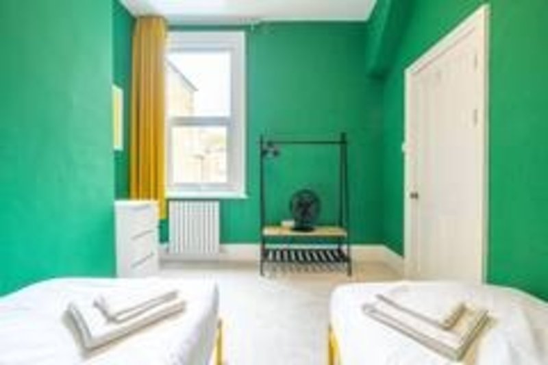 Bright green bedroom with two twin beds, window with yellow curtains, and trampoline