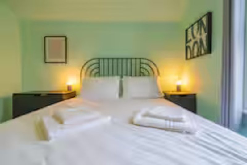 Bedroom with double bed, green headboard, white bedding, and wall-mounted lights