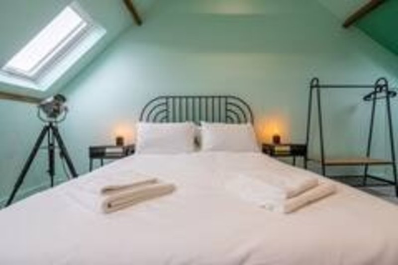 Modern attic bedroom with metal bed frame, skylights, tripod lamps and rolled towels