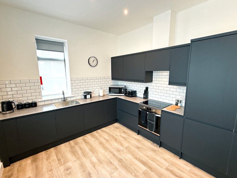 Modern kitchen with dark cabinetry, white subway tile backsplash, wooden flooring and integrated appliances