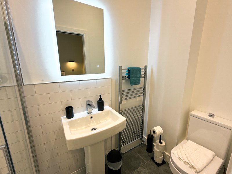 Modern bathroom with pedestal sink, illuminated mirror, heated towel rail and toilet