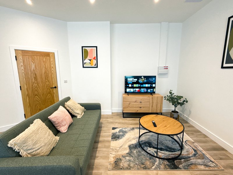 Modern living room with green sofa, wooden coffee table, TV unit, and wall art