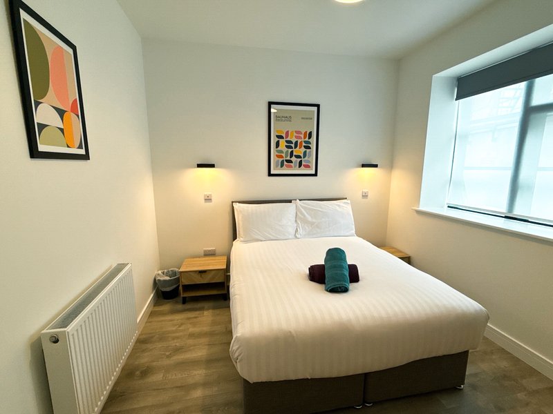Modern bedroom with double bed, white bedding, wall art, bedside lamps and wooden floor