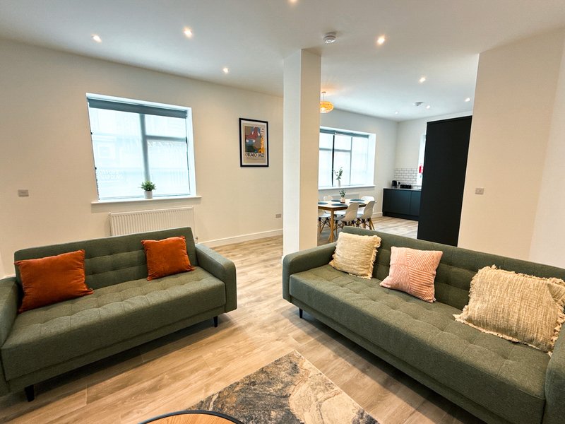 Modern living room with two green sofas, orange cushions, wooden flooring and recessed ceiling lights