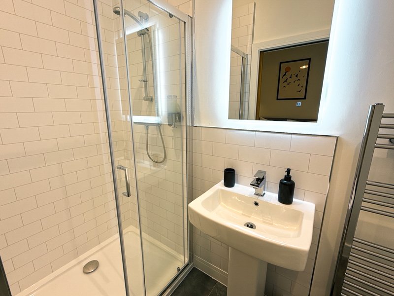 Modern bathroom with white subway tile, glass shower enclosure, pedestal sink and mirror