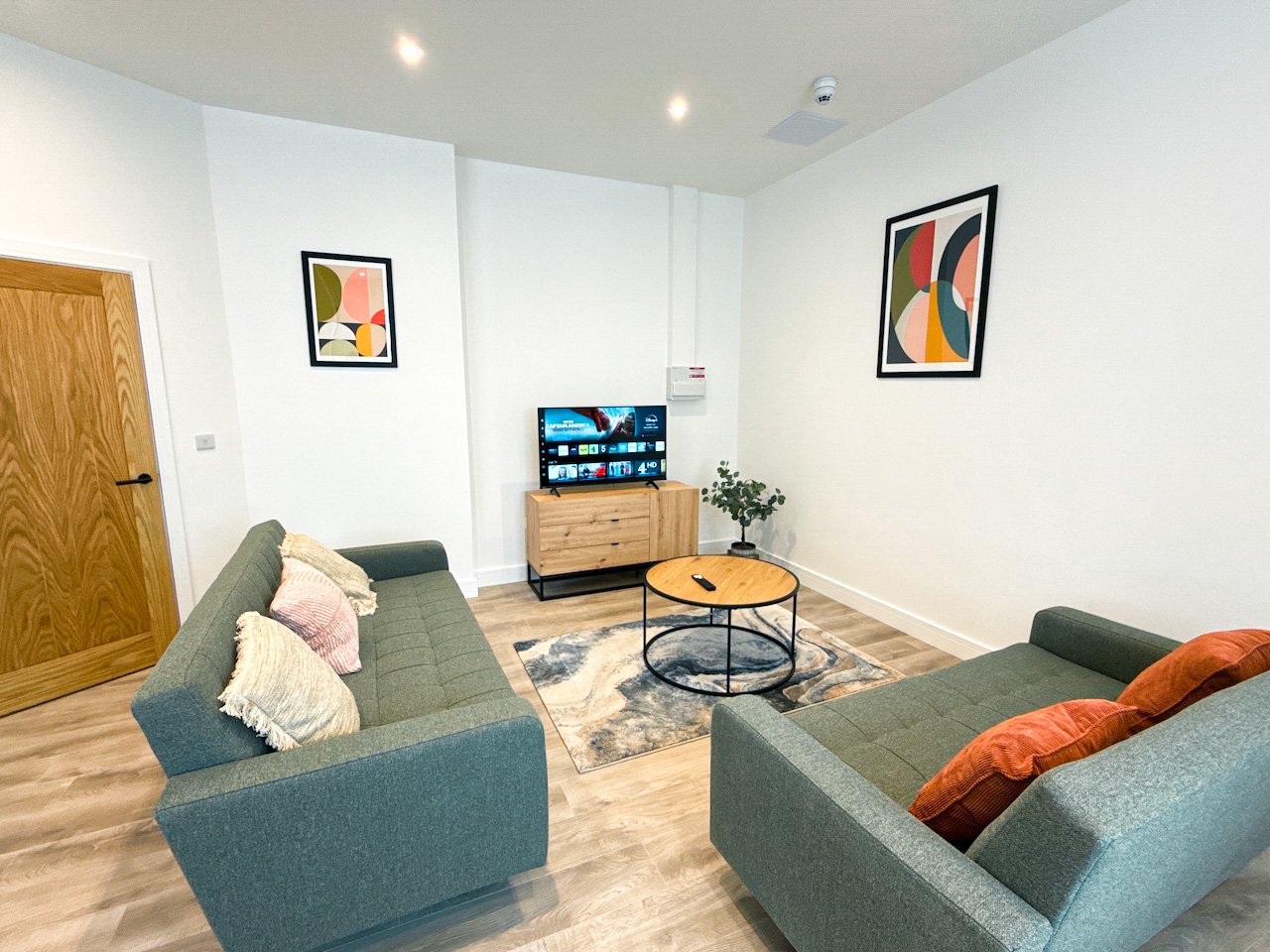 Modern living room with two teal sofas, wooden coffee table, TV, and abstract wall art