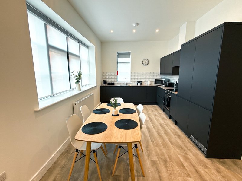 Modern kitchen with dining table, black cabinetry, wooden floor and large window