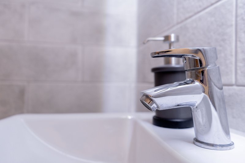 Modern bathroom sink with chrome tap and white ceramic basin, tiled wall background