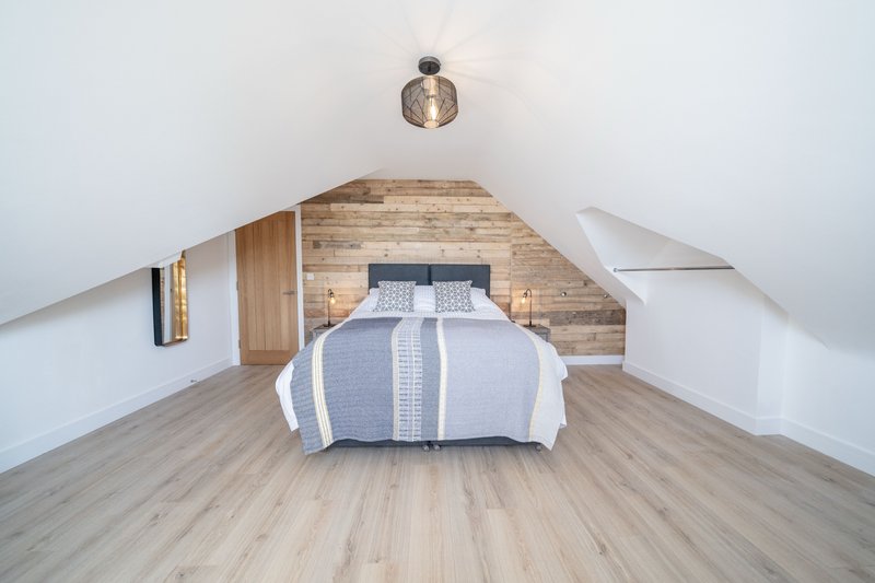 Attic bedroom with double bed, wooden headboard, pendant light and sloped ceiling