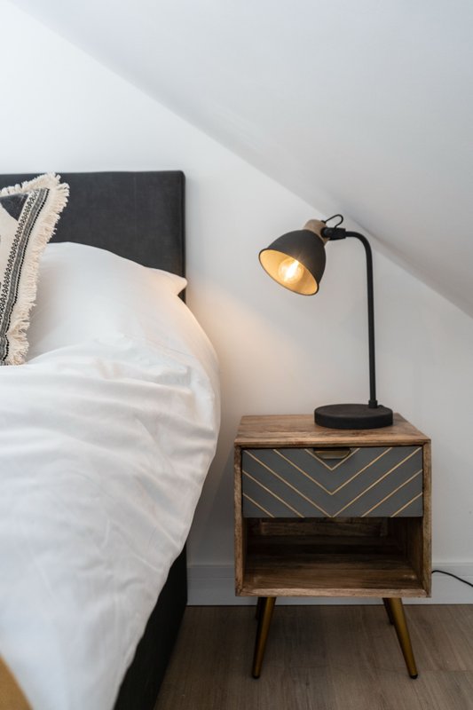 Bedroom with double bed, dark headboard, wooden nightstand with lamp