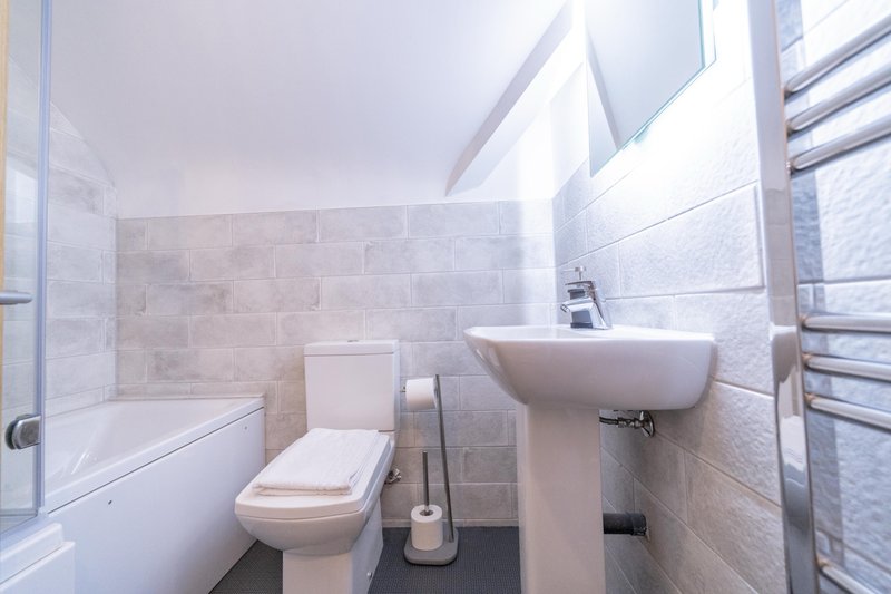 Modern bathroom with toilet, pedestal sink, bathtub, and heated towel rail