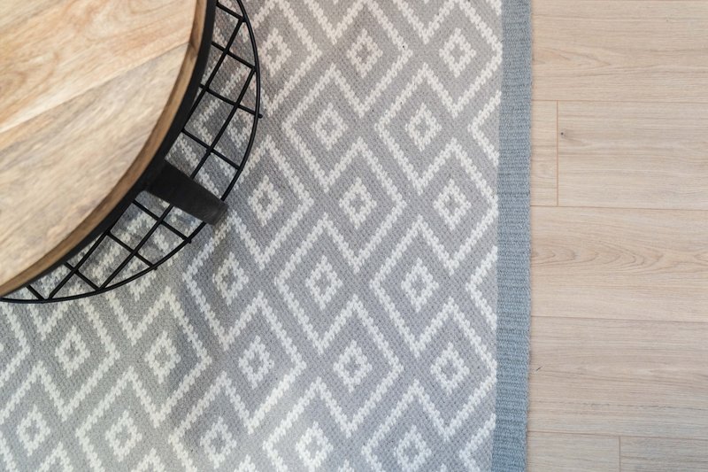 Light wood flooring with geometric patterned gray and white area rug and round black side table