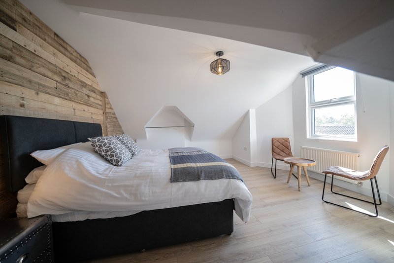Modern attic bedroom with double bed, wooden accent wall, two chairs and window