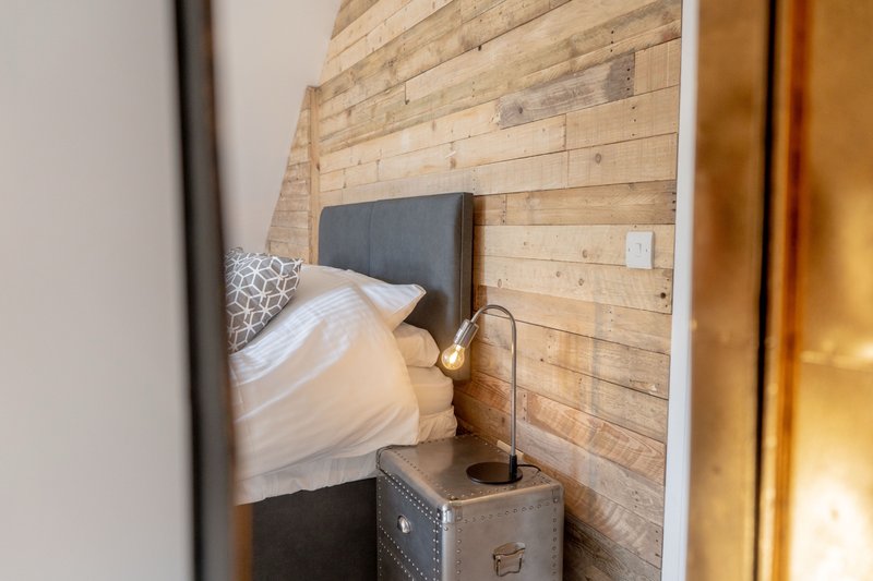 Compact bedroom with wooden feature wall, single bed and bedside storage trunk