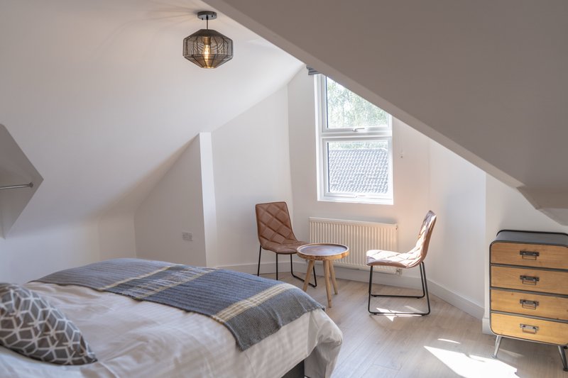 Bright attic bedroom with double bed, two chairs, wooden chest of drawers and skylight window