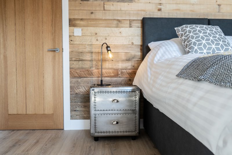 Bedroom with double bed, wooden wall, studded bedside table and patterned cushions