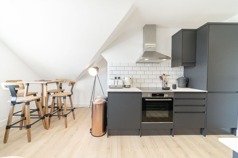 Modern kitchenette with dark cabinets, white subway tile backsplash, wooden bar seating area and light flooring