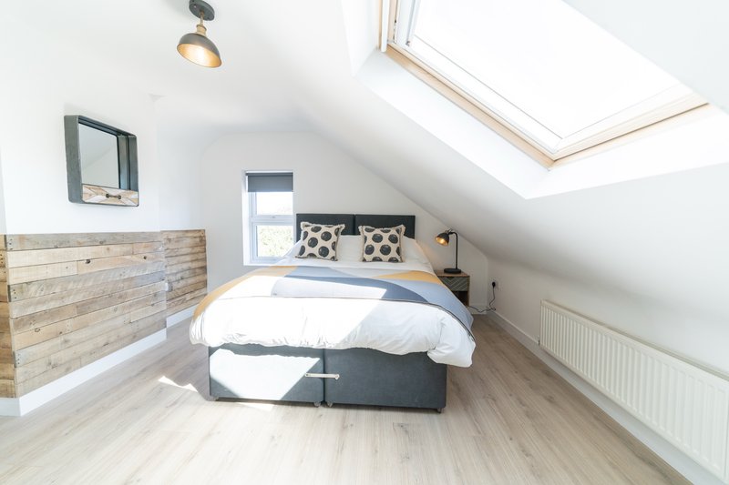 Bright attic bedroom with double bed, wooden headboard, skylight and pendant lamp