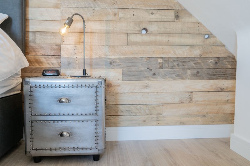 Industrial-style bedside table with drawers, gooseneck lamp, and wooden accent wall