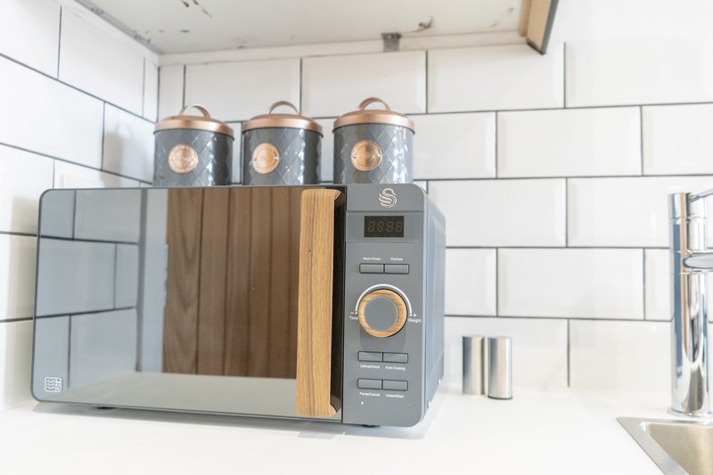 Modern kitchen counter with gray microwave, wooden accents, metal canisters and white subway tiles