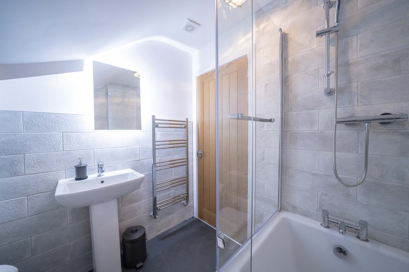 Modern bathroom with pedestal sink, walk-in shower, heated towel rail and illuminated mirror
