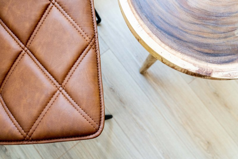 Close-up of quilted brown leather bag and decorative plate on light wooden surface