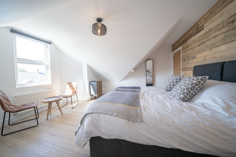 Bright attic bedroom with double bed, wooden accent wall, chair, and sloped ceiling
