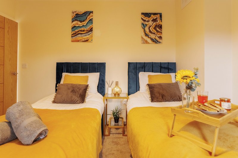 Twin bedroom with yellow bedding, dark headboards, abstract wall art, and shared nightstand