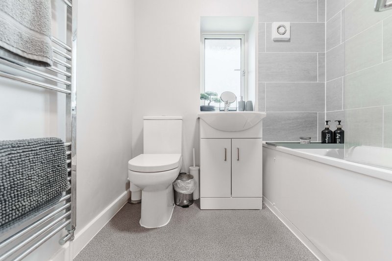 Modern bathroom with toilet, vanity sink, bathtub, heated towel rail and window