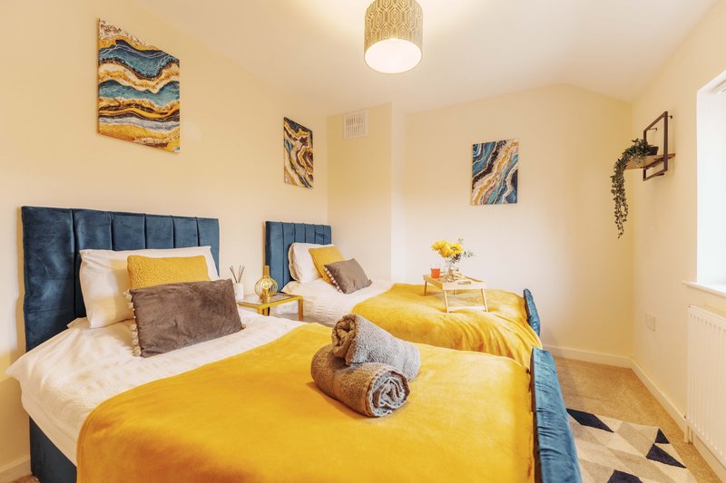 Bright bedroom with two double beds, yellow bedding, blue headboards and framed wall art