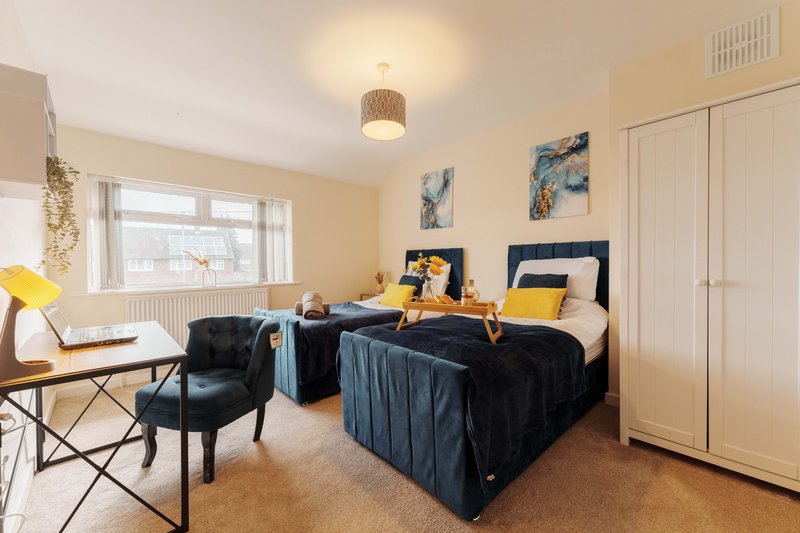 Bright bedroom with two single beds, desk, chair, and large windows with natural light