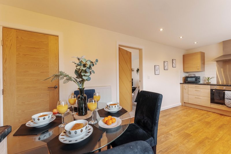 Open-plan kitchen and dining area with wooden doors, dining table set with plates and orange fruit, black chair visible