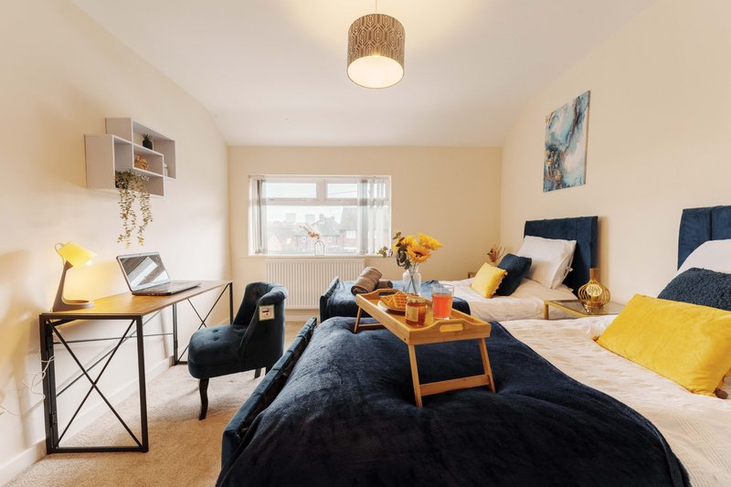 Bright bedroom with two beds, wooden furniture, desk area, and yellow accent cushions