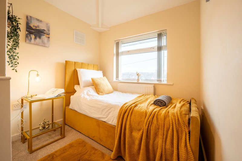 Bright yellow bedroom with single bed, wooden nightstand, table lamp and window view