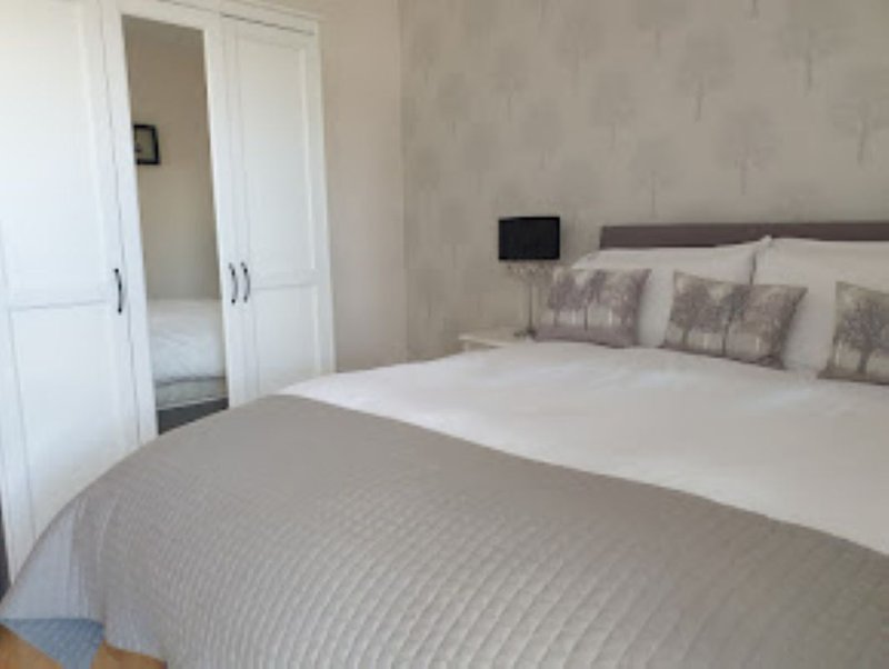Bedroom with double bed, grey bedding, decorative cushions, and built-in wardrobes