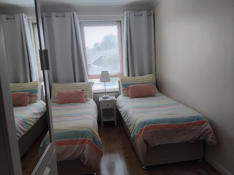 Bedroom with two single beds, striped bedding, nightstand, lamp and windows with curtains