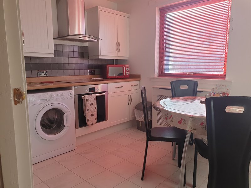 white kitchen with white appliances, dining table, and window with blinds.