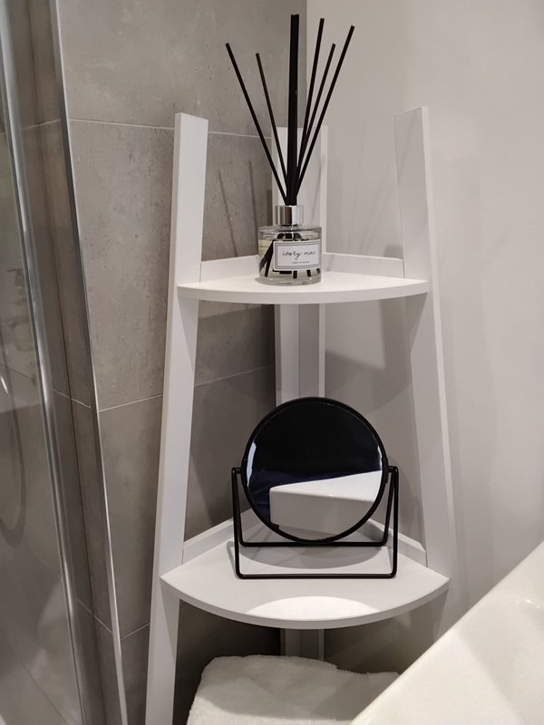 White corner shelf unit with reed diffuser and black decorative mirror in bathroom