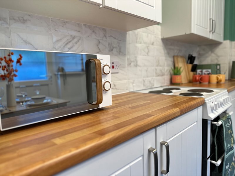 Modern kitchen with white cabinetry, marble backsplash, wooden countertop and microwave