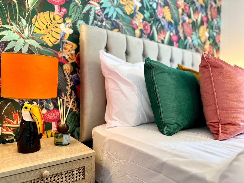 Bedroom with upholstered headboard, colorful pillows, bedside table with lamp and plant