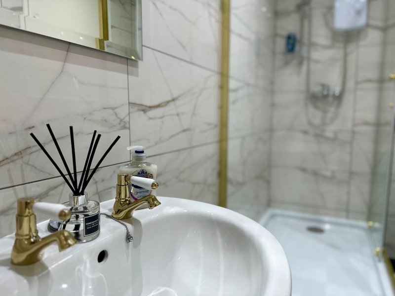 Modern bathroom sink with marble tile backsplash, brass faucet, and glass shower enclosure