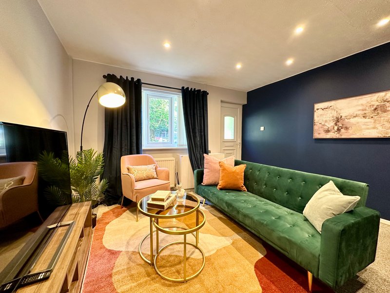 Modern living room with green velvet sofa, orange armchair, gold side table and dark blue accent wall