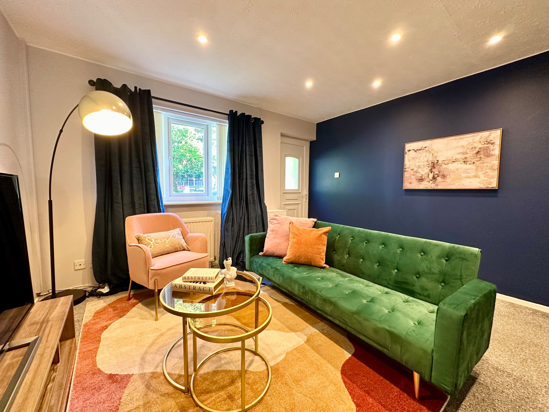 Modern living room with green sofa, orange armchair, arc lamp, and colorful area rug
