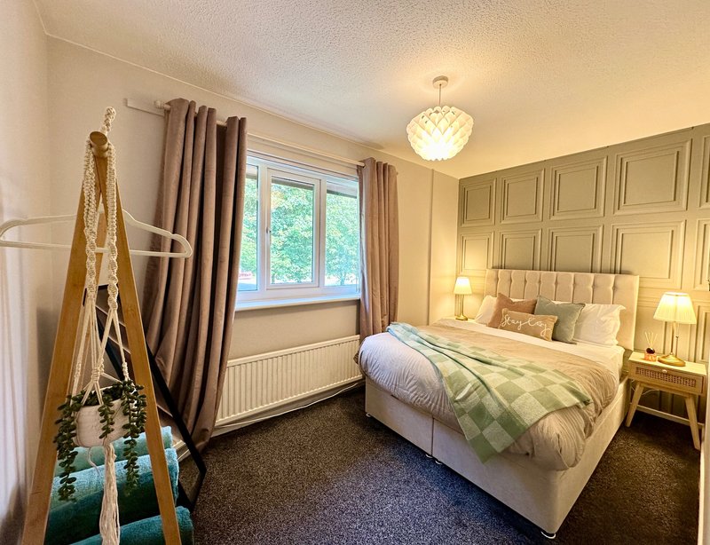 Bright bedroom with double bed, wooden headboard, window, curtains and bedside lamps