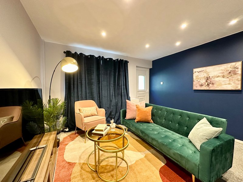 Modern living room with green velvet sofa, yellow armchair, arc lamp and navy accent wall
