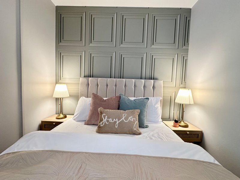 Bedroom with upholstered headboard, decorative pillows, bedside lamps, and panelled wall feature