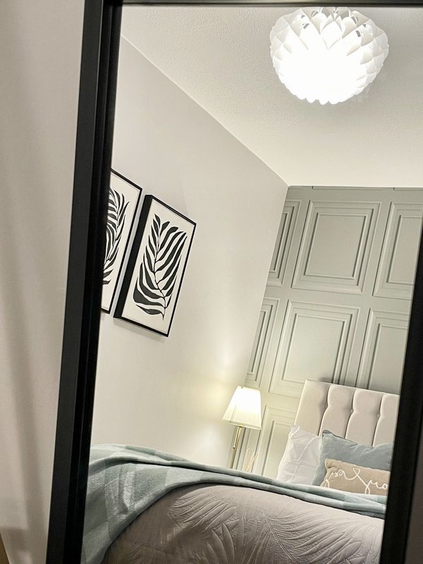 Bedroom mirror reflection showing bed, headboard, wall art, ceiling light and wardrobe