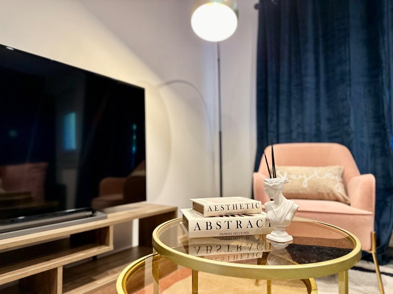 Modern living room with TV, peach armchair, gold coffee table, and blue curtains