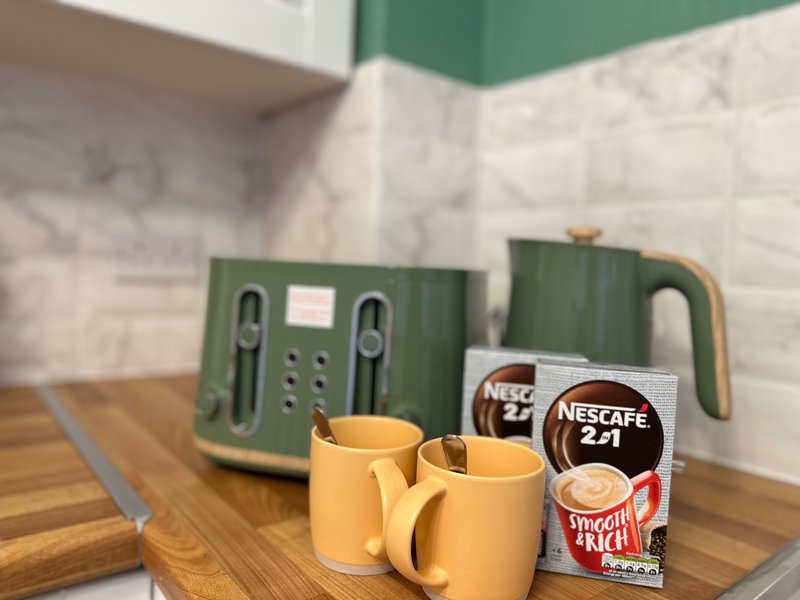 Kitchen counter with green kettle, toaster, yellow mugs and coffee products